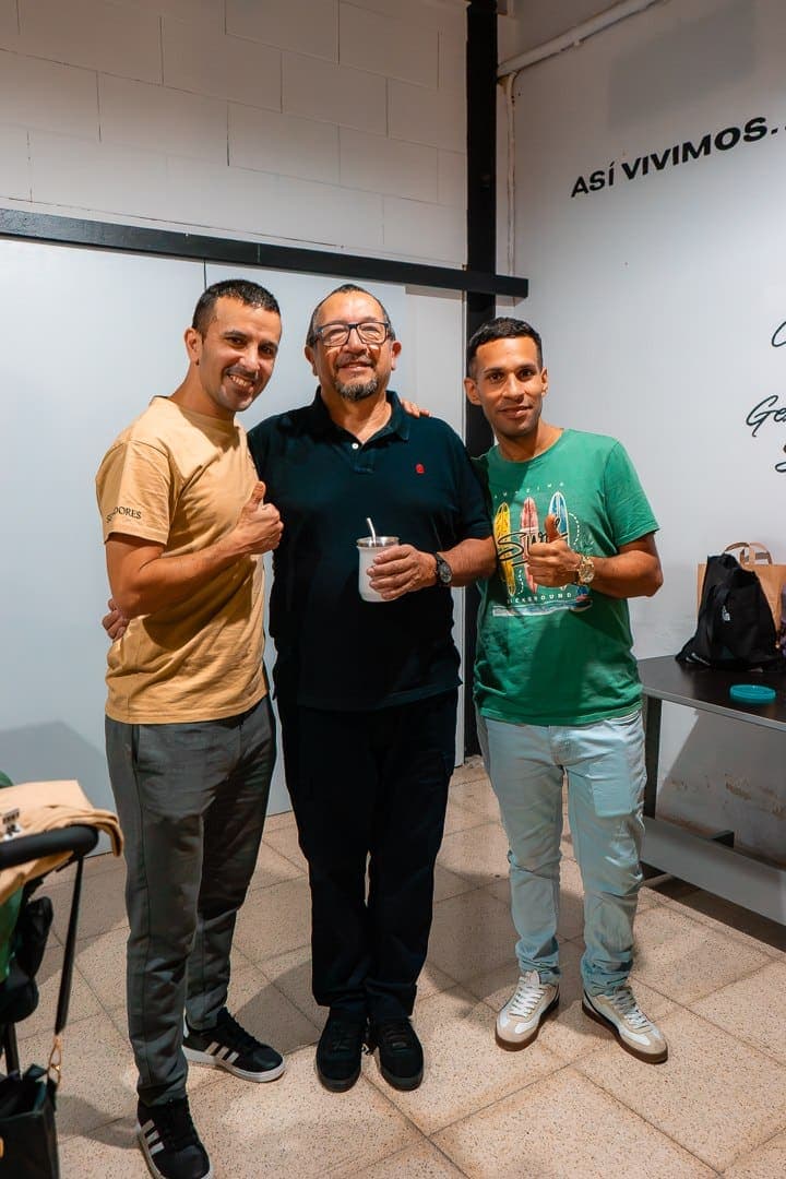 Tres hombres de la iglesia abrazados y sonriendo junto a la pared donde se lee «Así vivimos»