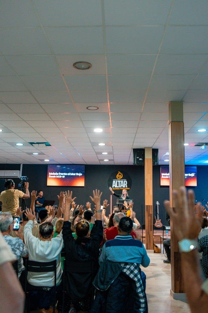 La sala llena durante una predicación, con la mayoría de los asistentes de pie y con las manos levantadas