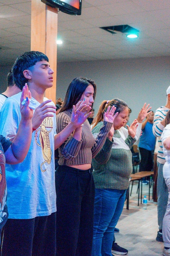 Varios asistentes de pie, en oración, con las manos levantadas y los ojos cerrados